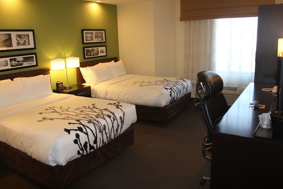 Habitación de hotel con dos camas, un escritorio, una silla y una ventana con cortinas.