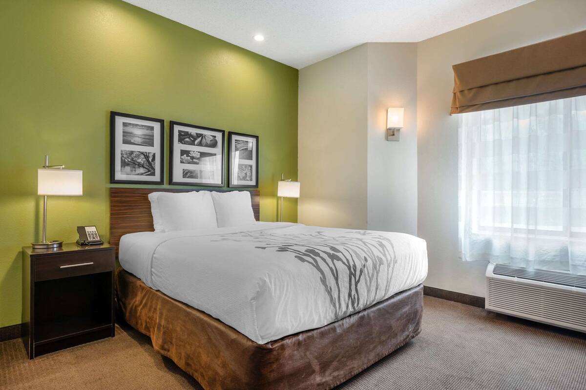 A hotel room with a large bed, two bedside tables with lamps, a wall-mounted phone, and framed pictures.