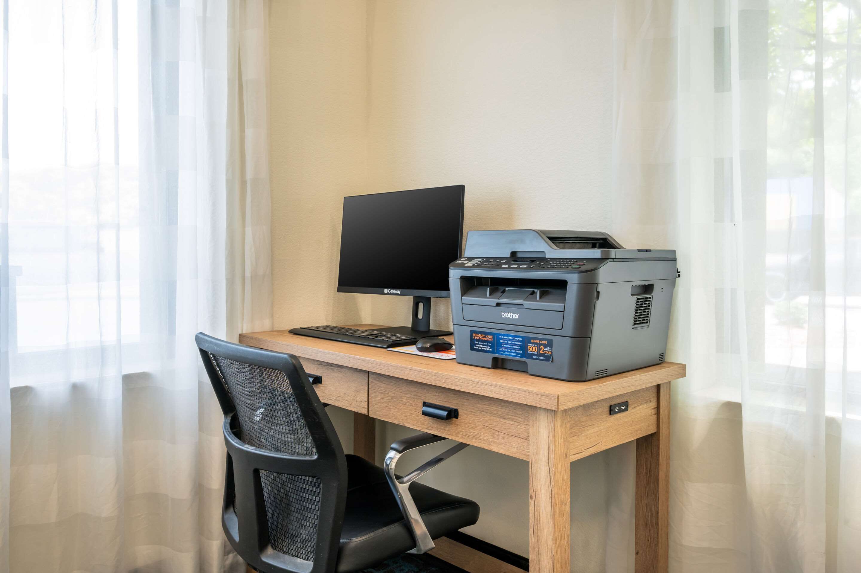 Un escritorio con un monitor de computadora, teclado e impresora Brother.