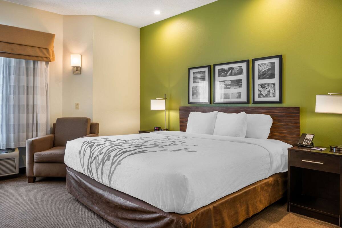 A hotel room with a large bed, a chair, a nightstand with a lamp, and three framed pictures on the wall.