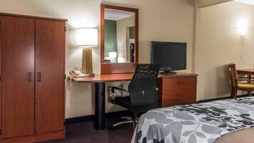 A hotel room with a wooden wardrobe, a desk with a telephone, a chair, a television, and a bed with a floral bedspread.