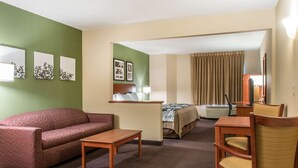 A hotel room with a sofa, a small table, a wooden chair, a bed, a desk, and a mirror.