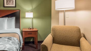 Habitació d'hotel amb un llit, una taula de nit amb una làmpada i una butaca estampada.