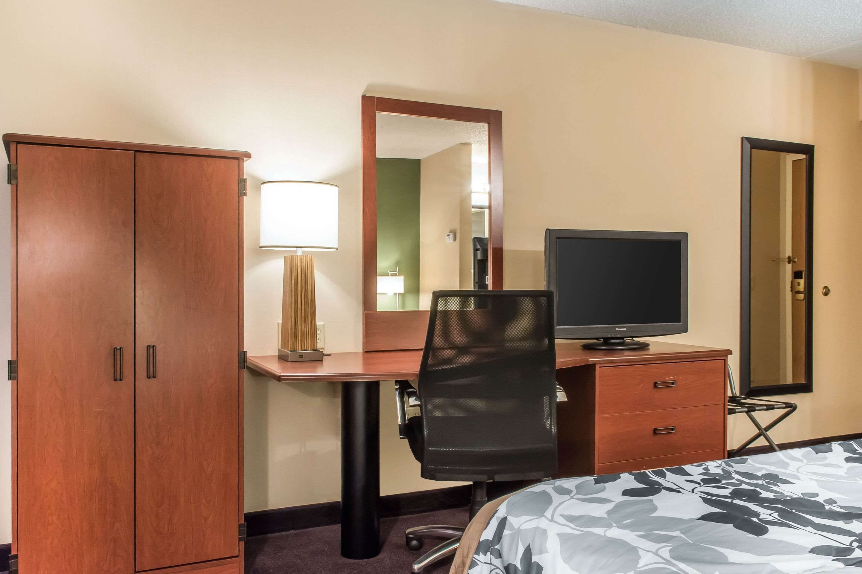 Habitación de hotel con un armario de madera, un escritorio con una silla, un televisor y una cama con colcha estampada.