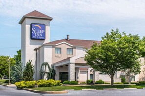 A Sleep Inn & Suites building with a prominent sign, a covered entrance, and a landscaped front yard with various shrubs and trees.