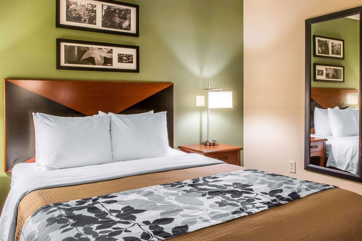 A hotel room with a bed, a nightstand, a lamp, a mirror, and framed pictures on the wall.