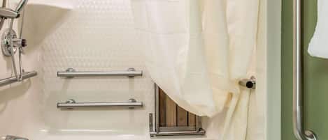 Una bañera con cabezal de ducha, barras de apoyo y una ventana.