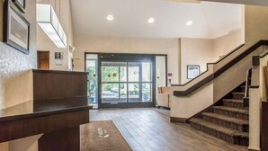 A reception area with a wooden floor, a reception desk, a staircase, and a door leading outside.