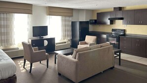 Habitación de hotel con cama, sofá, televisión, refrigerador, microondas y kitchenette.