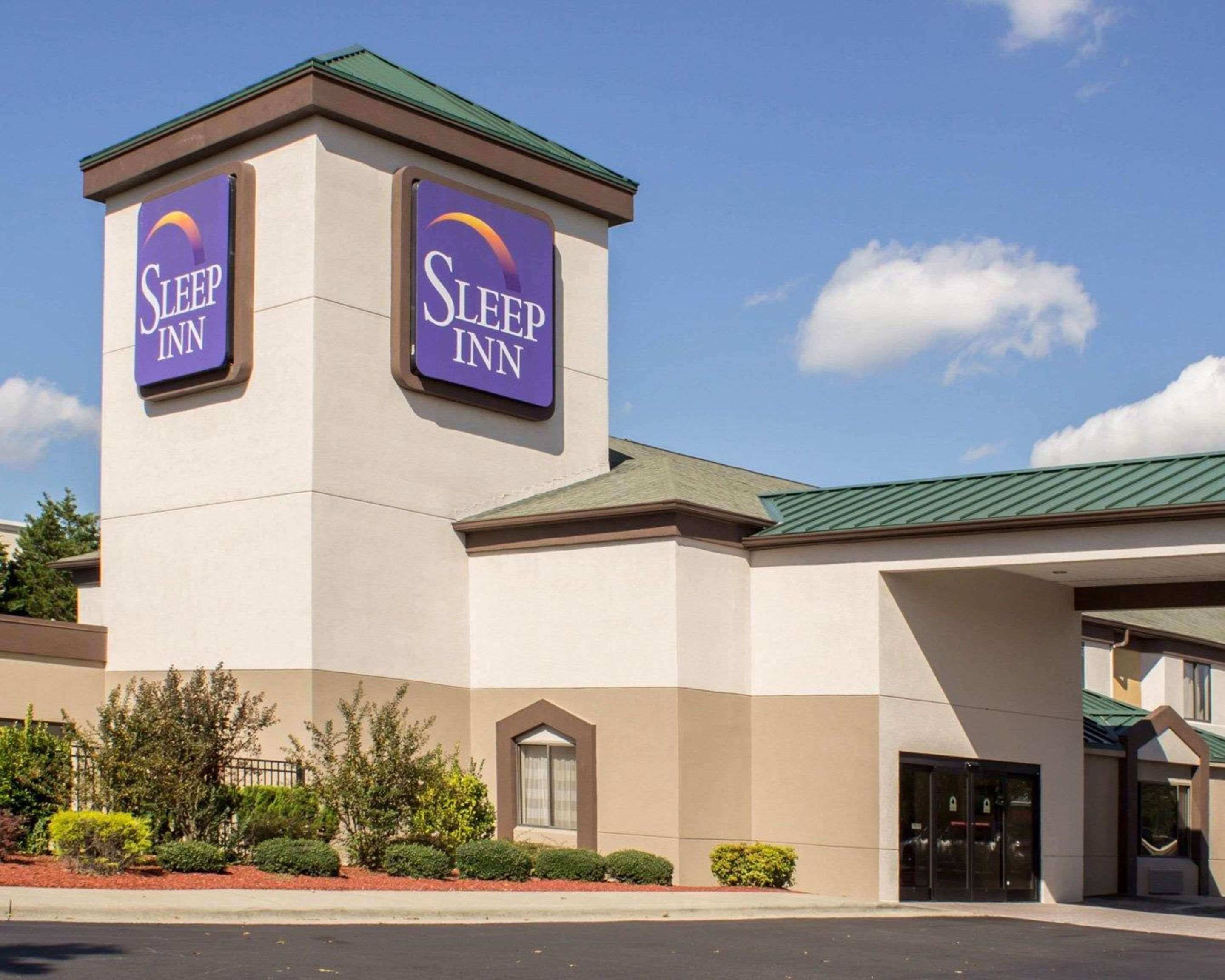 A Sleep Inn hotel with a prominent tower featuring two signs, a main entrance, and a parking lot.