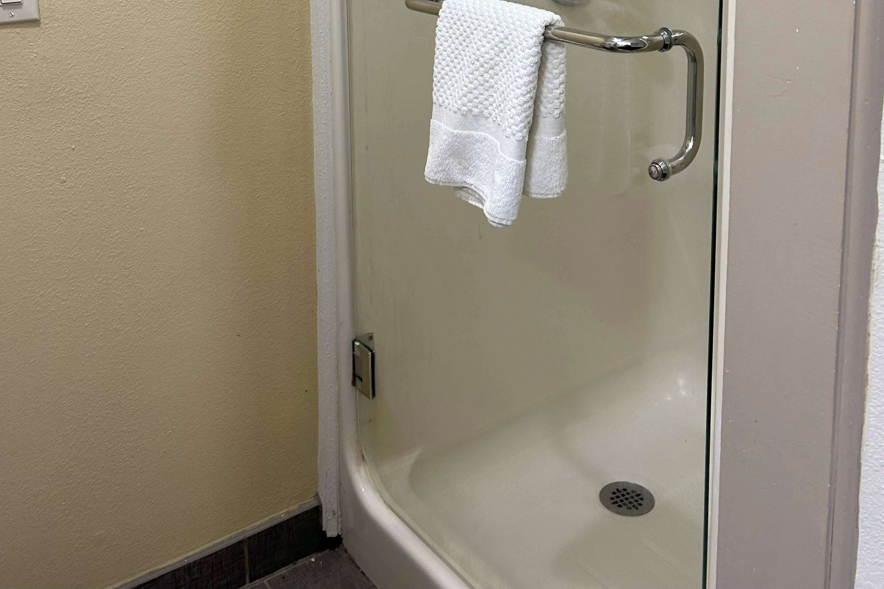 Zona de ducha con puerta de cristal, barra de apoyo metálica y una toalla blanca colgada del pomo.