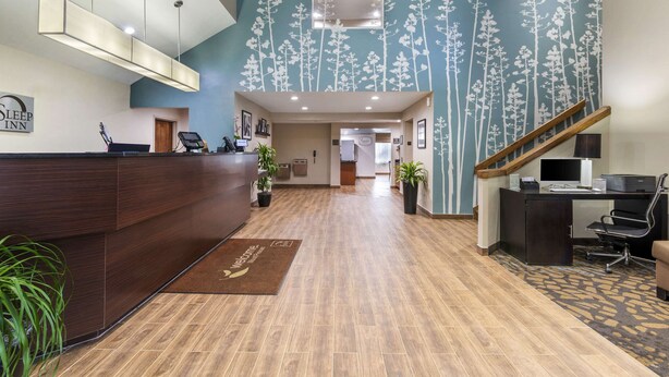 A hotel reception area with a wooden reception desk, a digital screen, and a wall-mounted sign. - Sleep Inn Mt. Pleasant - Charleston (Mount Pleasant)