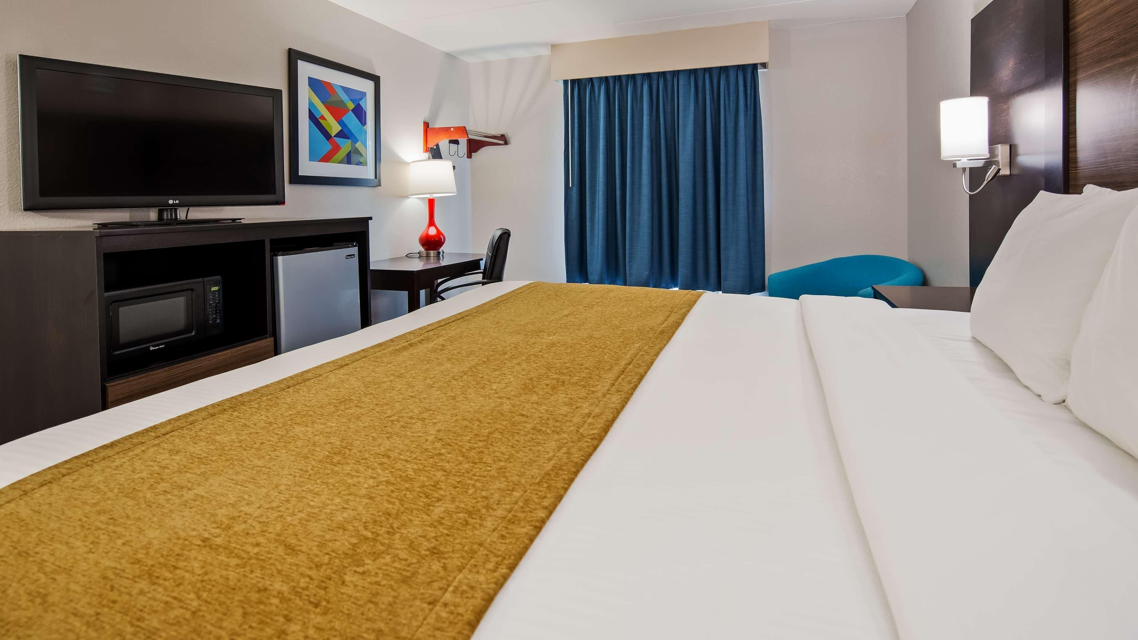 A hotel room with a bed, a desk with a computer, a television, a microwave, and a refrigerator.