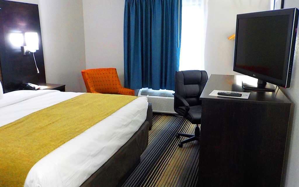 Una habitación de hotel con una cama, un escritorio con computadora, una silla y un televisor.