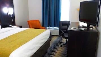 Una habitación de hotel con una cama, un escritorio con computadora, una silla y un televisor.