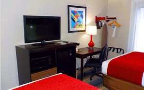 A hotel room with a TV, desk, chair, and two beds.
