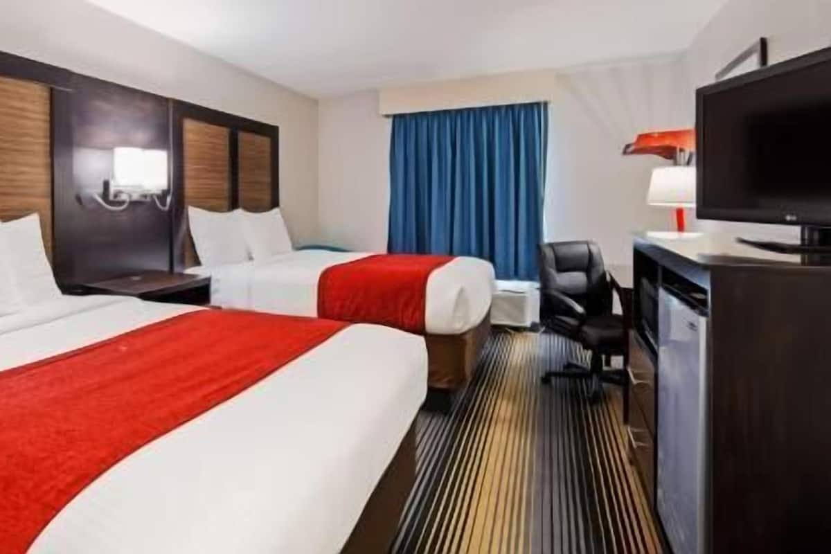 Une chambre d’hôtel avec deux lits, un bureau, une chaise, une télévision et une fenêtre avec des rideaux bleus.