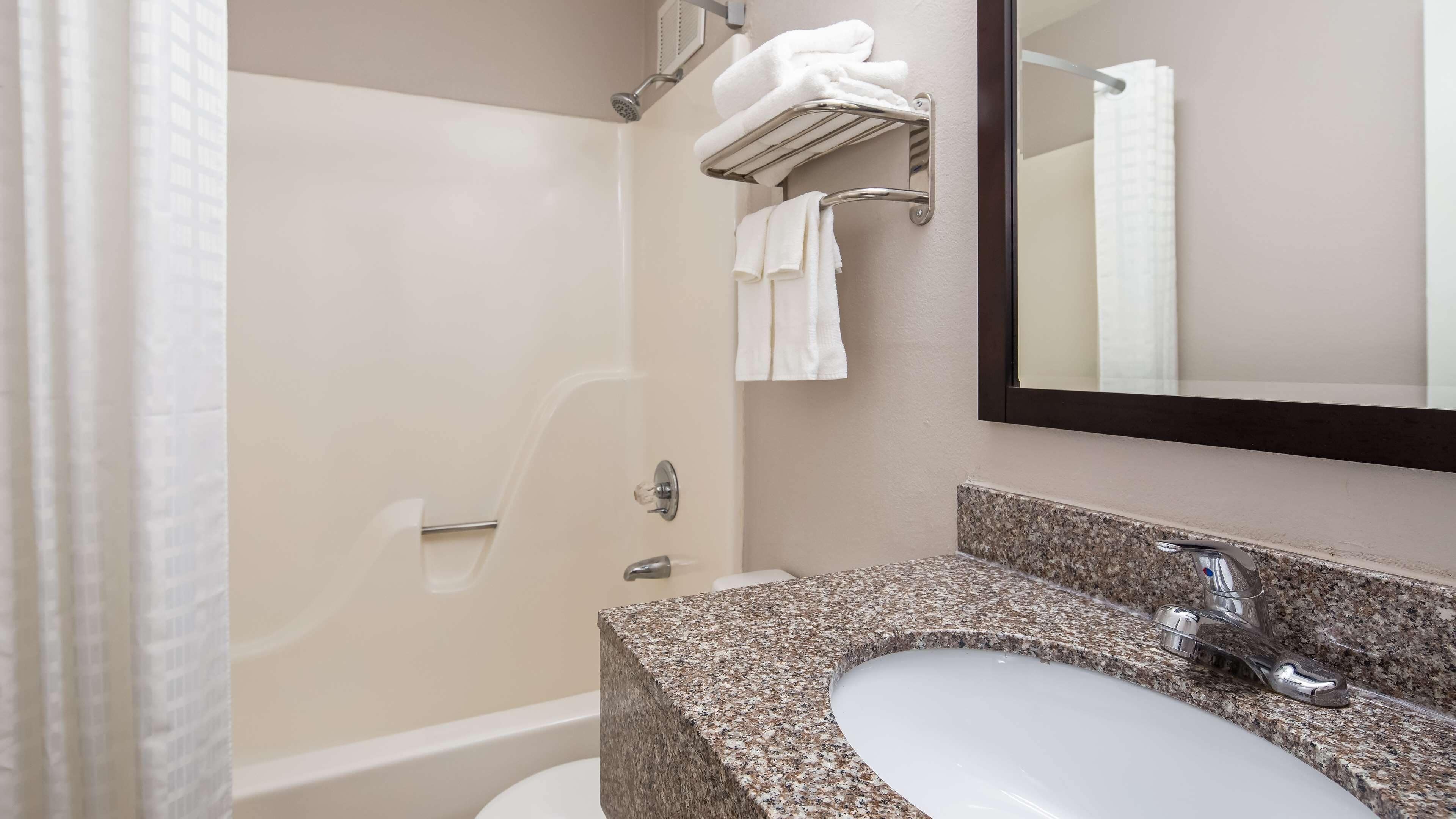 A bathroom with a granite countertop sink, a mirror, a towel rack, and a shower.