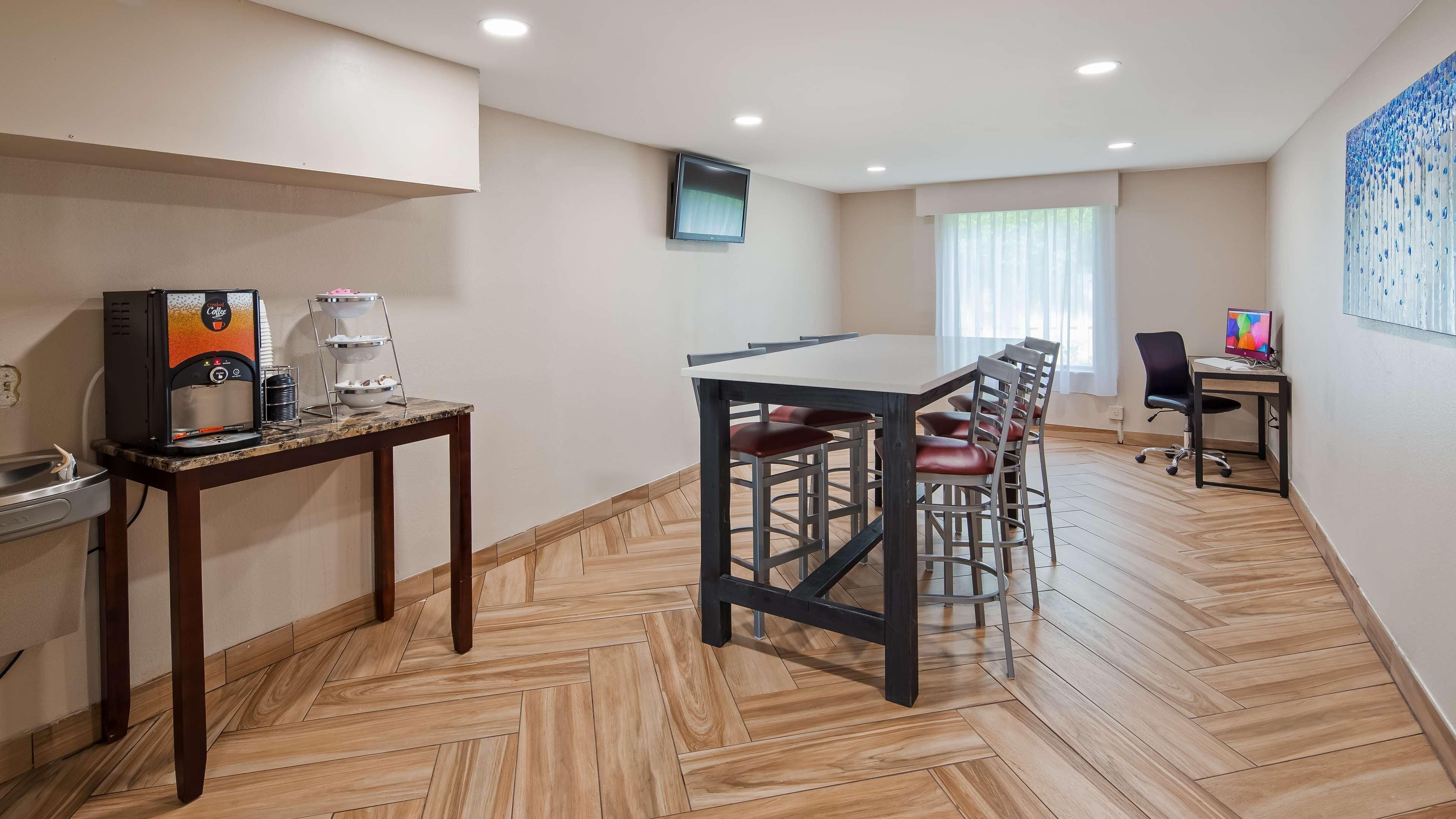 Una habitación de hotel moderna con comedor, cafetera, televisor y escritorio con computadora.