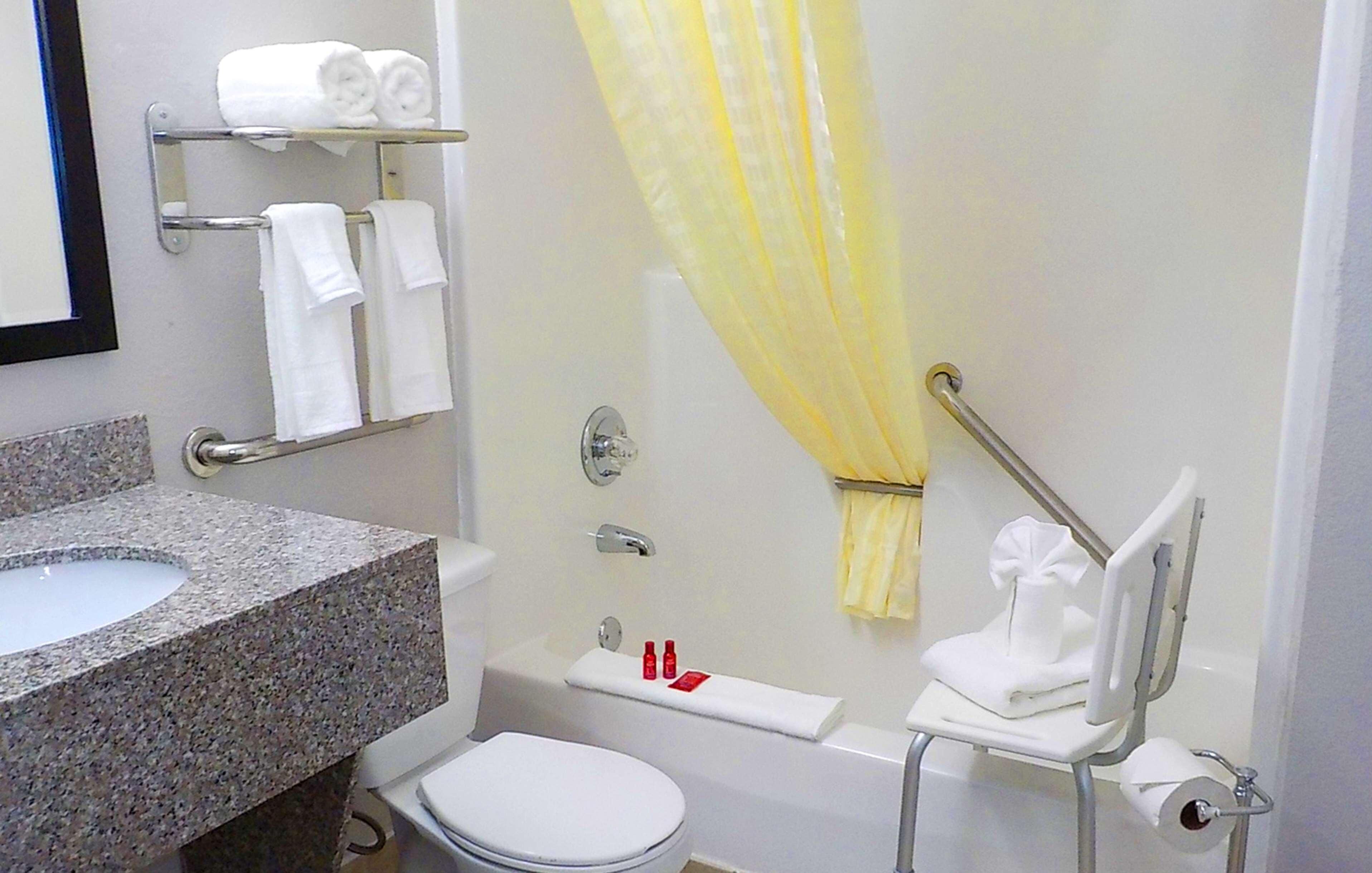 A bathroom with a granite sink, white toilet, and a shower with a yellow shower curtain.