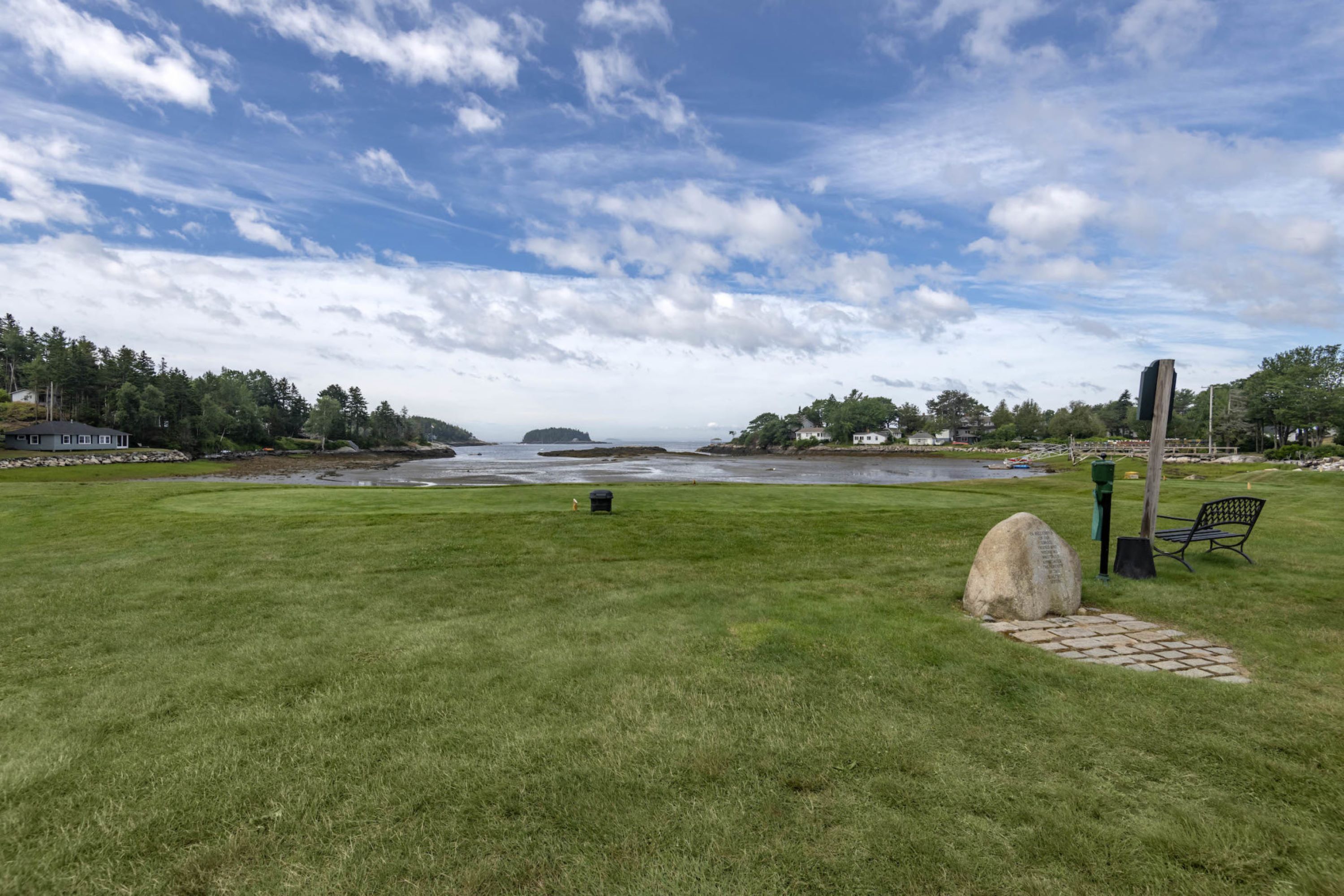 A grassy field with a stone pathway leading to a bench and a wooden post.