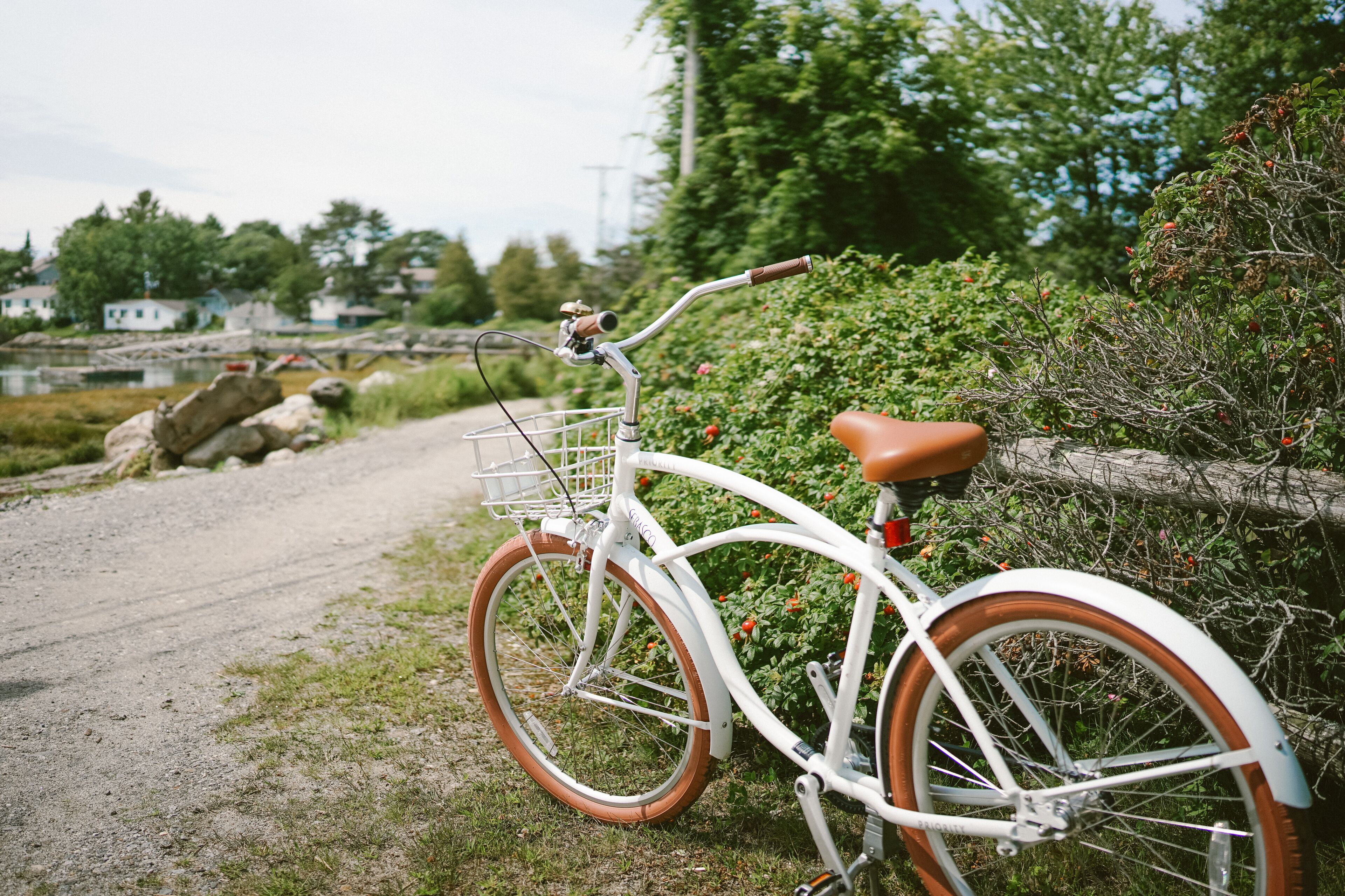 Un vélo blanc avec des détails marron est garé sur un chemin de gravier, à côté d’une clôture en bois.