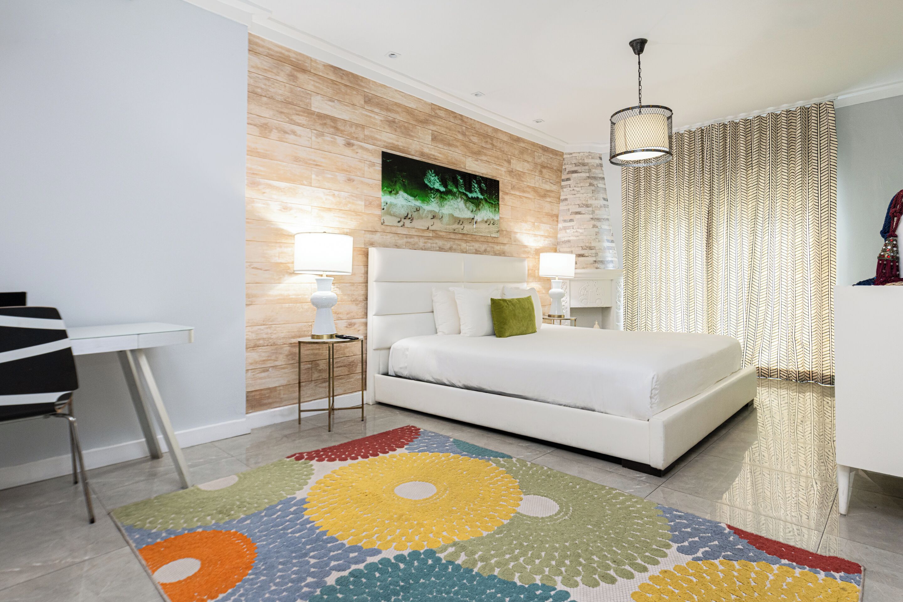 A modern bedroom with a white bed, a wooden accent wall, a colorful rug, and a desk with a chair.