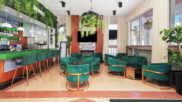 A modern bar area with green upholstered chairs, a bar counter, and a large TV screen. - Chesterfield Hotel & Suites (Miami Beach)