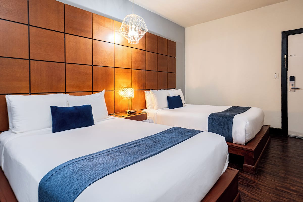 A hotel room with two beds, wooden headboard, bedside lamps, and a door.
