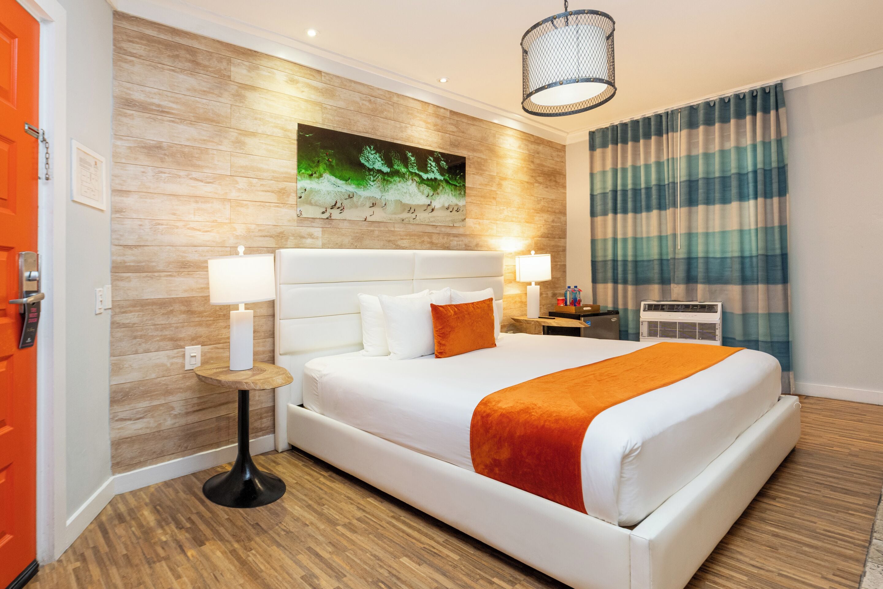 Een hotelkamer met een groot bed, twee bedlampen, een kunstwerk aan de muur en een gestreept gordijn.
