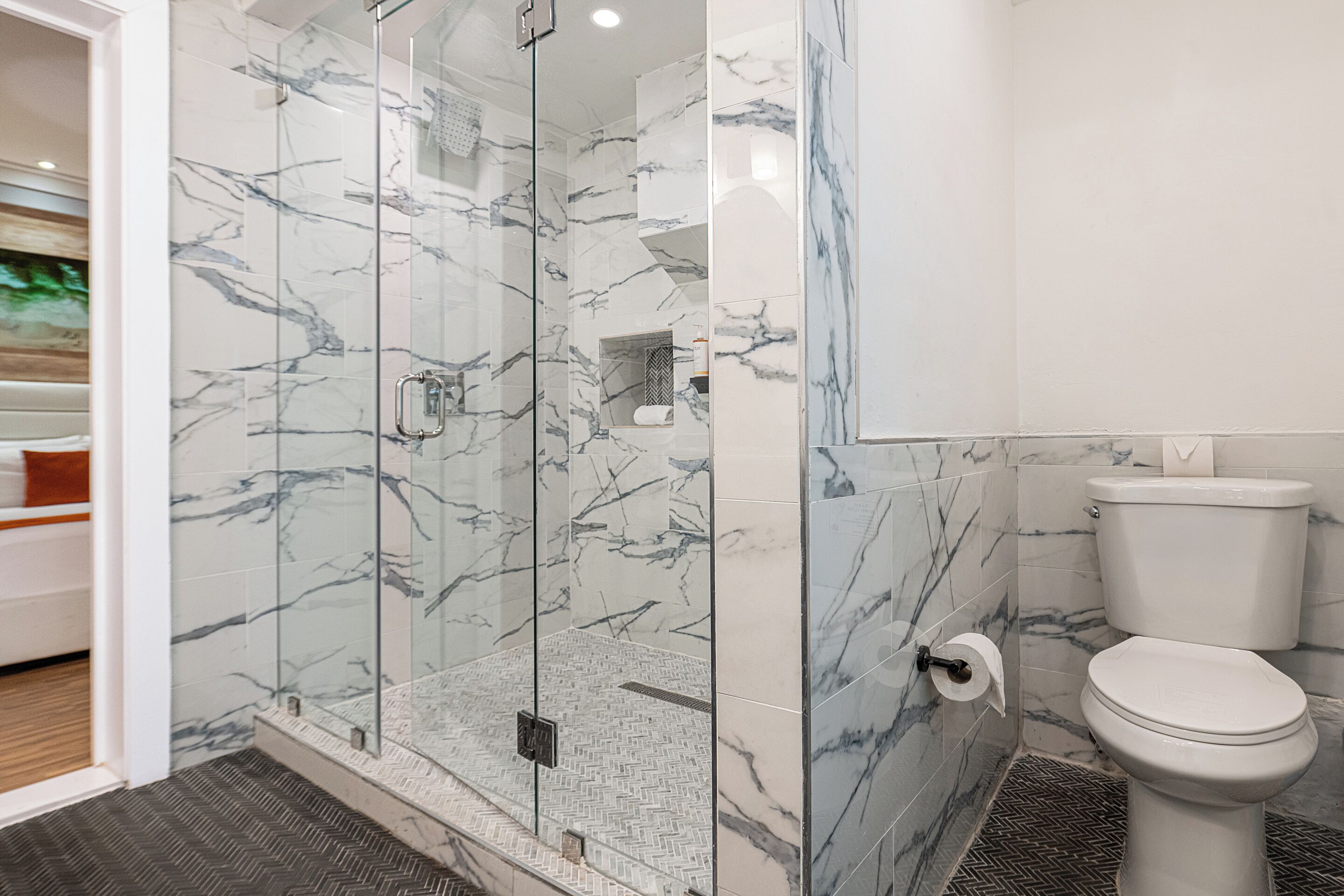 A modern bathroom with a glass-enclosed shower, a toilet, and a herringbone-patterned floor.