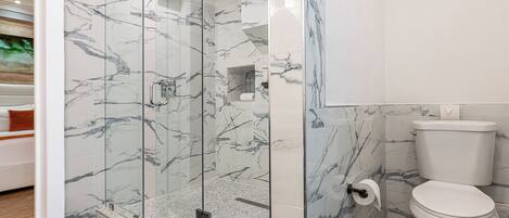 A modern bathroom with a glass-enclosed shower, a toilet, and a herringbone-patterned floor.