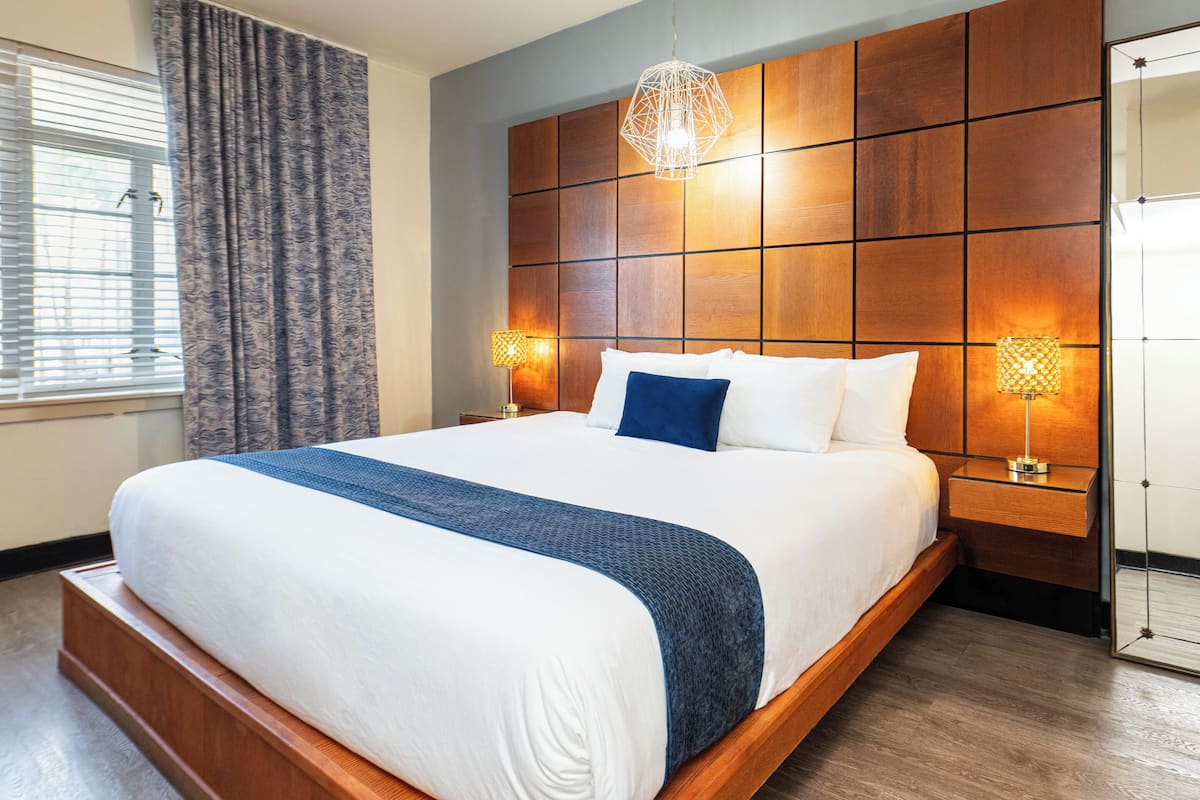 A large bed with a wooden headboard, two bedside lamps, and a window with curtains.