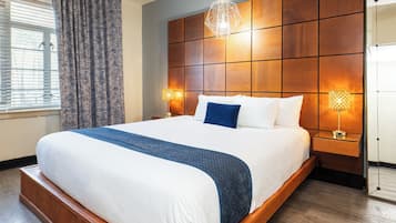 A large bed with a wooden headboard, two bedside lamps, and a window with curtains.
