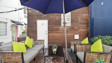 An outdoor seating area with wicker furniture, a central table, and a large umbrella.