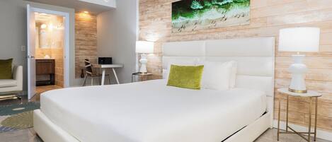 Quarto de hotel moderno com uma cama grande, uma parede de destaque em madeira, um quadro e uma pequena mesa com cadeira.