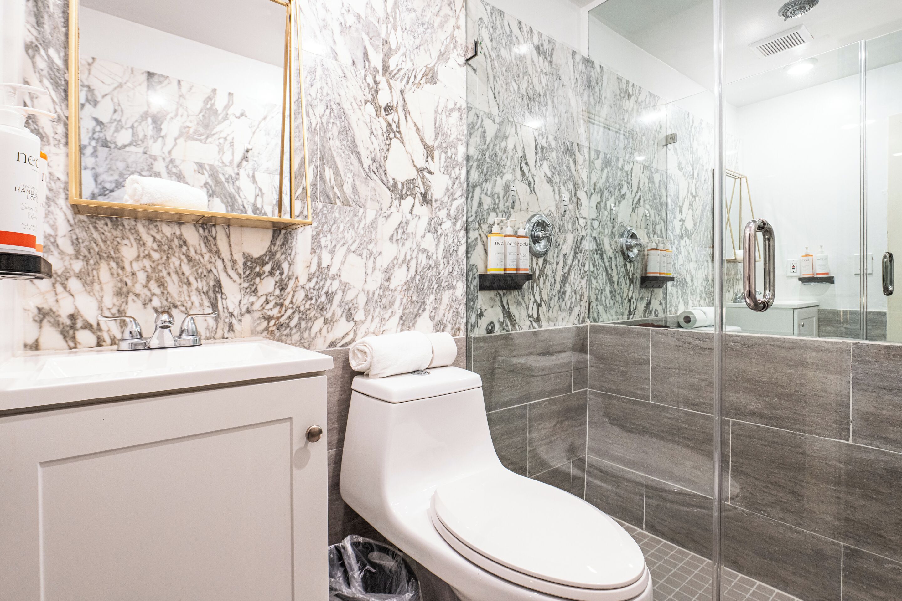 Ein Badezimmer mit Marmorwand, Toilette, Waschbecken und Duschbereich.