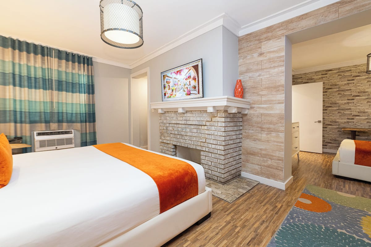 A hotel room with a bed, a fireplace, a painting, and a view of another room.