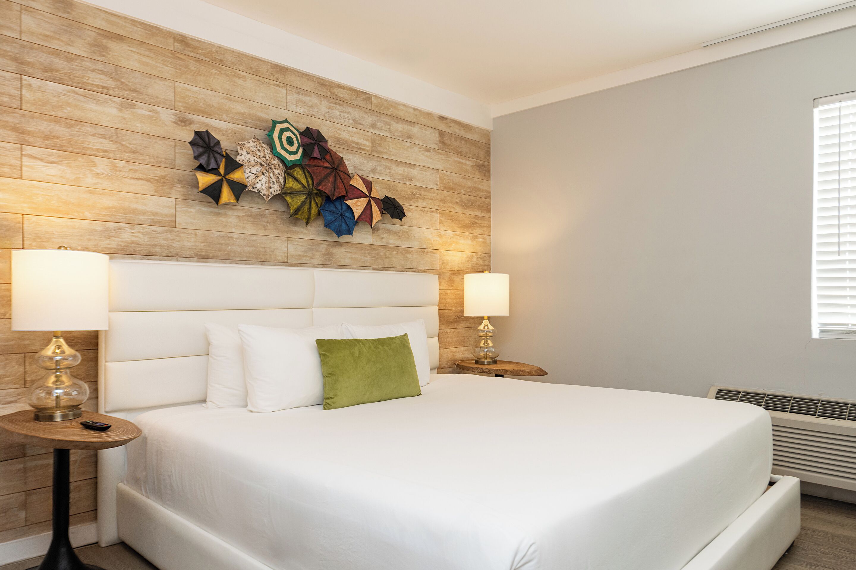 Habitación de hotel con cabecera de madera, una cama grande con ropa de cama blanca, dos mesitas de noche con lámparas y un adorno en la pared.