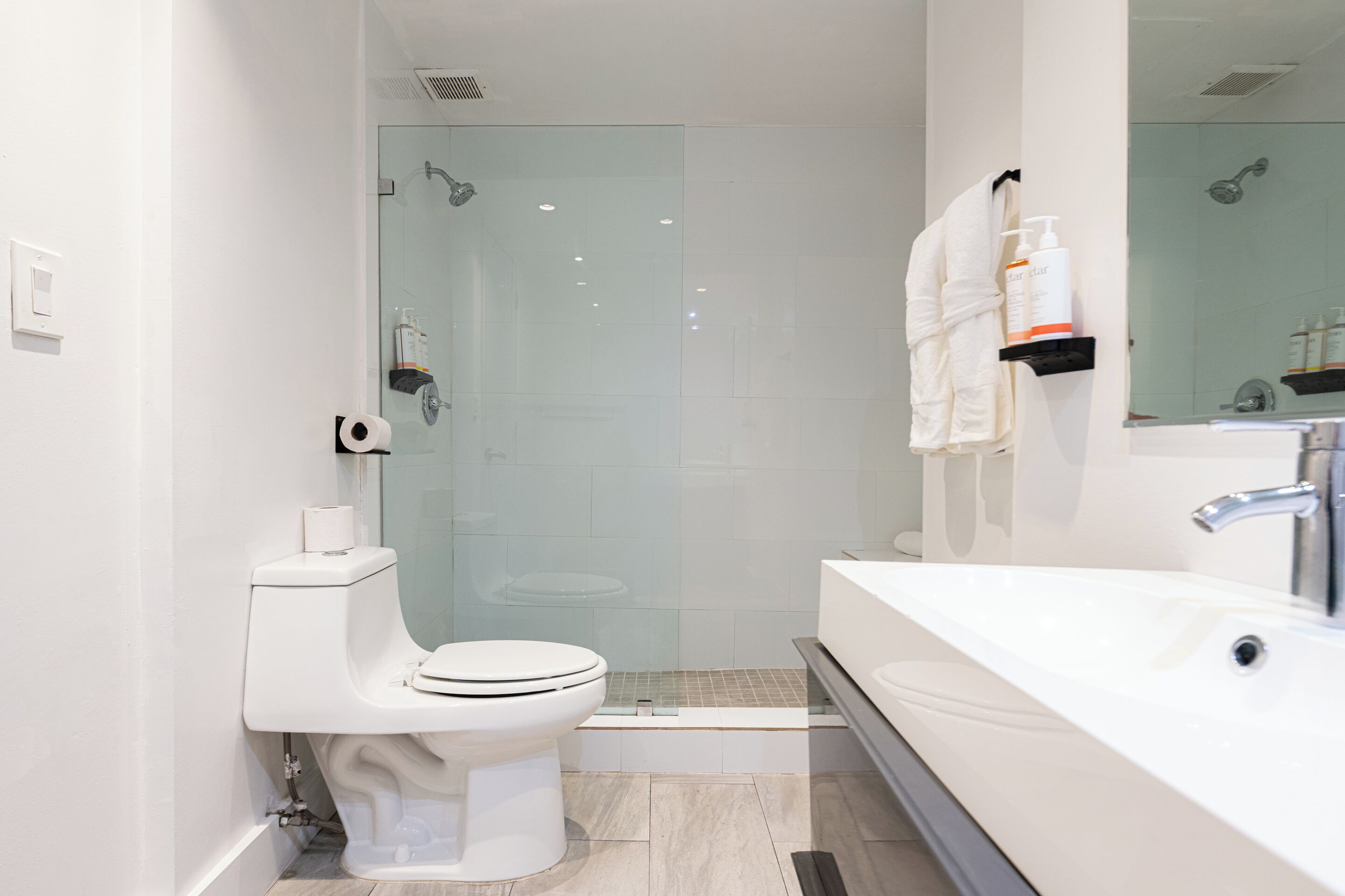 A modern bathroom with a glass-enclosed shower, a white toilet, and a large sink.