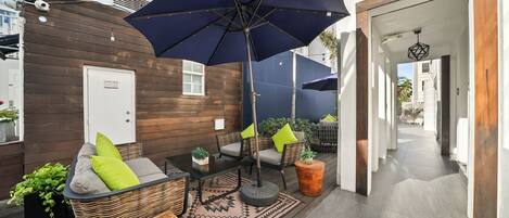 A patio area with wicker furniture, a large umbrella, and potted plants.
