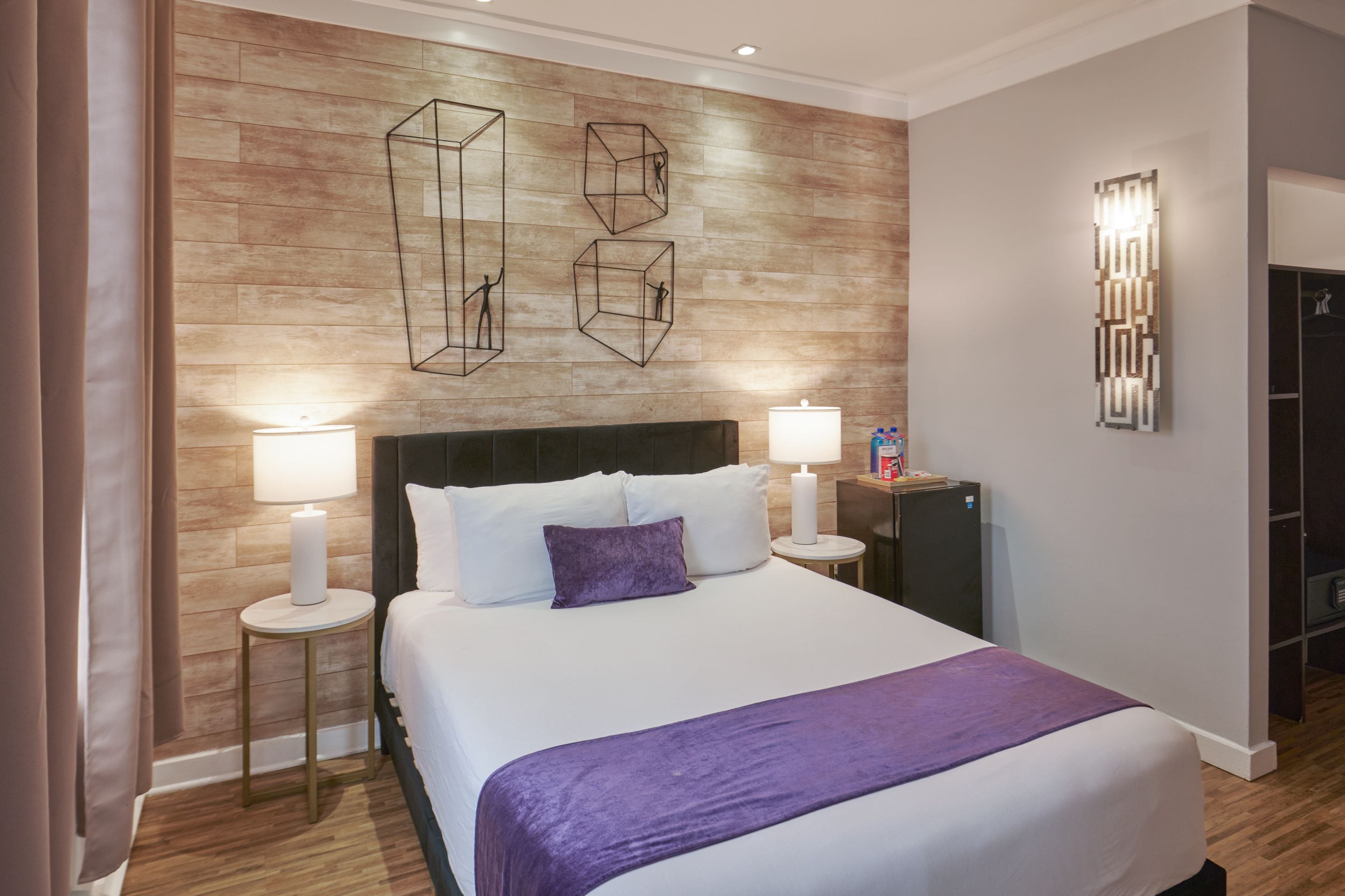 A hotel room with a bed, two bedside tables, a nightstand, a wall-mounted light fixture, and a wardrobe.