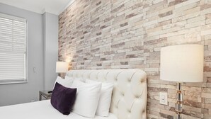 A bedroom with a tufted headboard, a white bed, and a modern lamp on a bedside table.