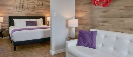 A hotel room with a bed, a white sofa, a round table, and a wall with geometric wall art.
