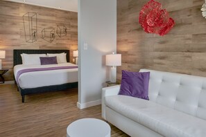 A hotel room with a bed, a white sofa, a round table, and a wall with geometric wall art. - Hotel Shelley (Miami Beach)