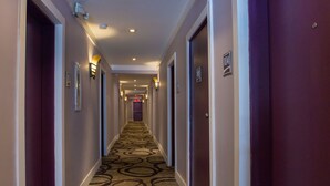 A hotel hallway with a patterned carpet, doors on both sides, and wall-mounted light fixtures.
