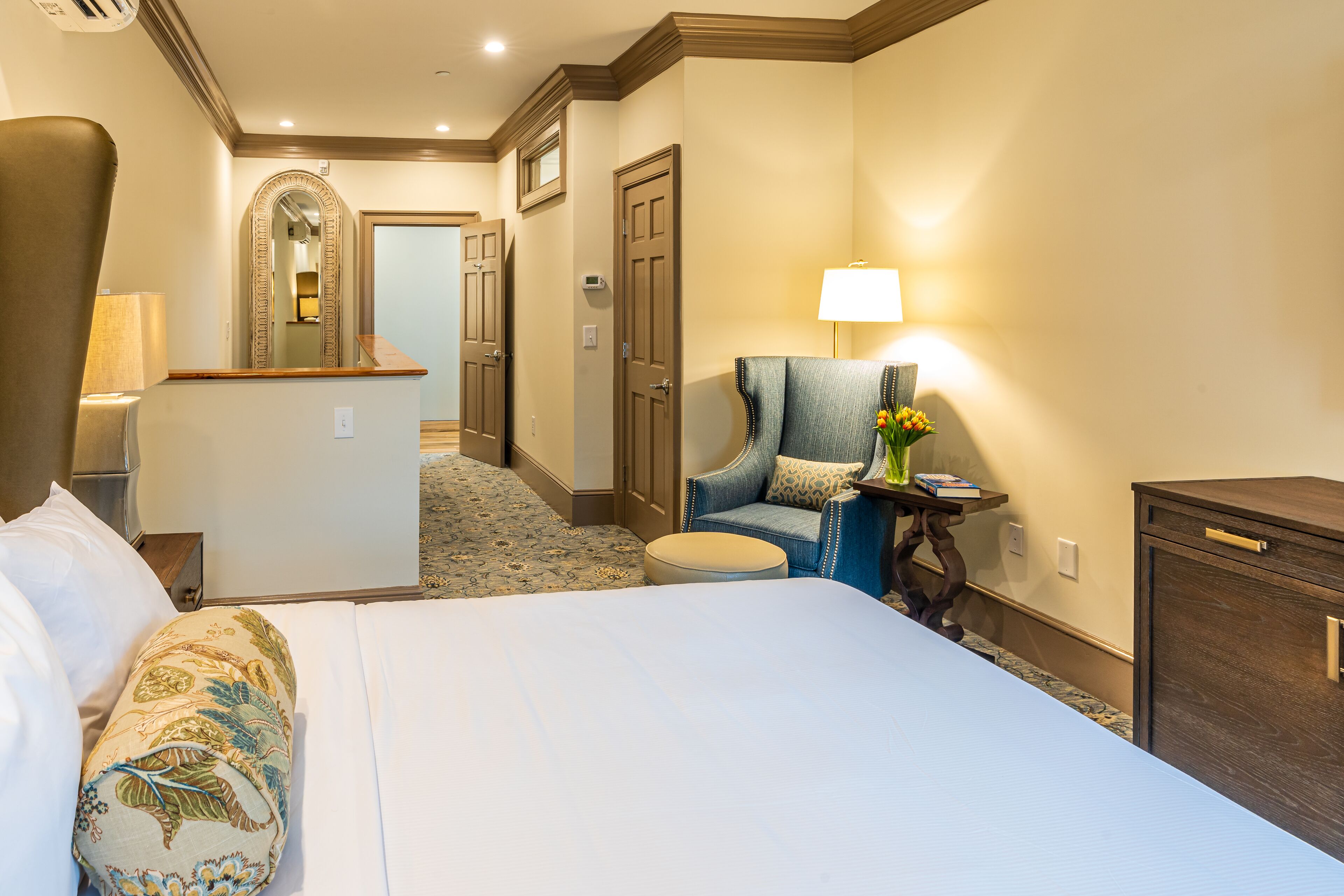 A hotel room with a large bed, a chair, a desk, and a mirror.
