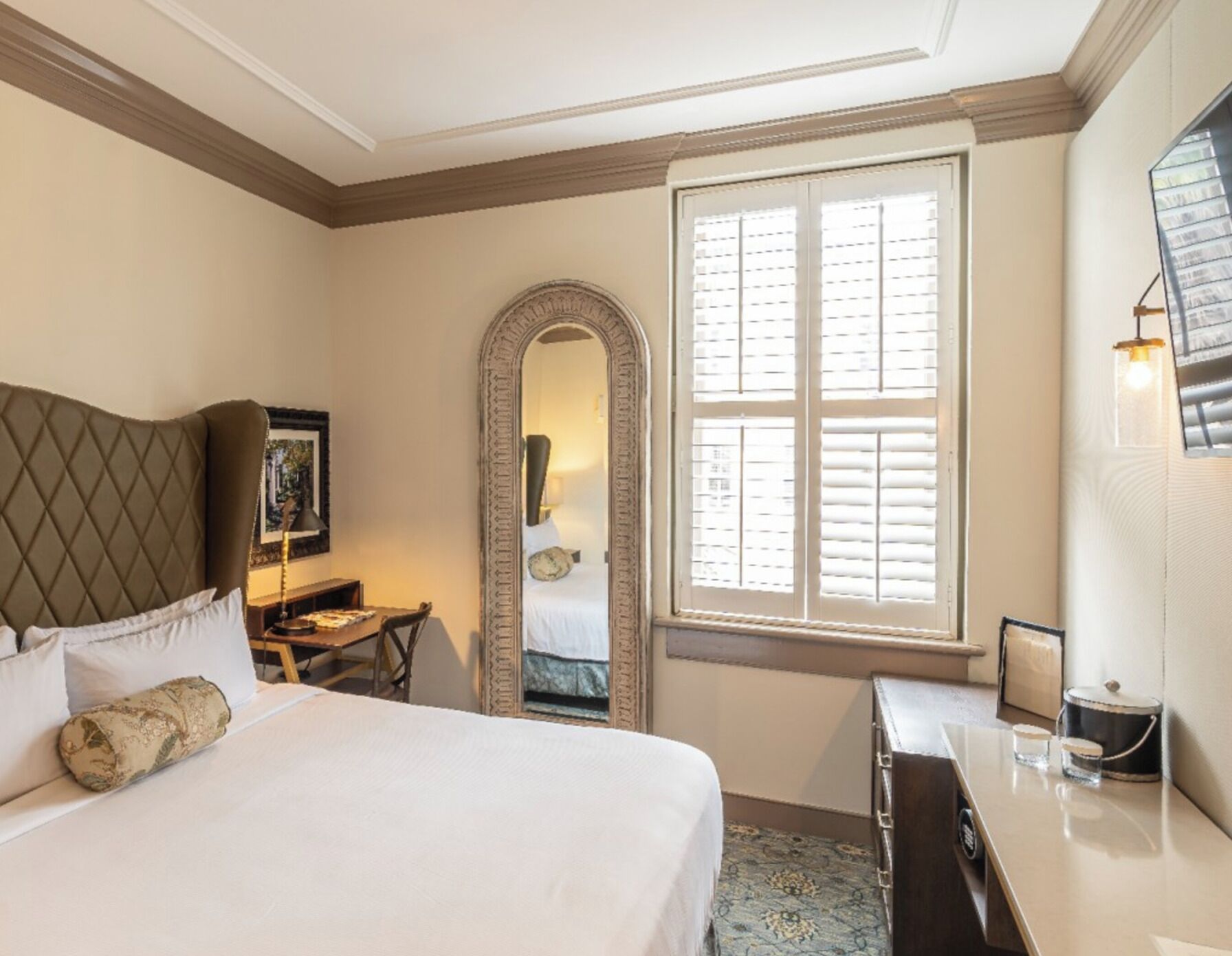 Une chambre d’hôtel avec un grand lit, un bureau, un miroir et une fenêtre avec des stores.