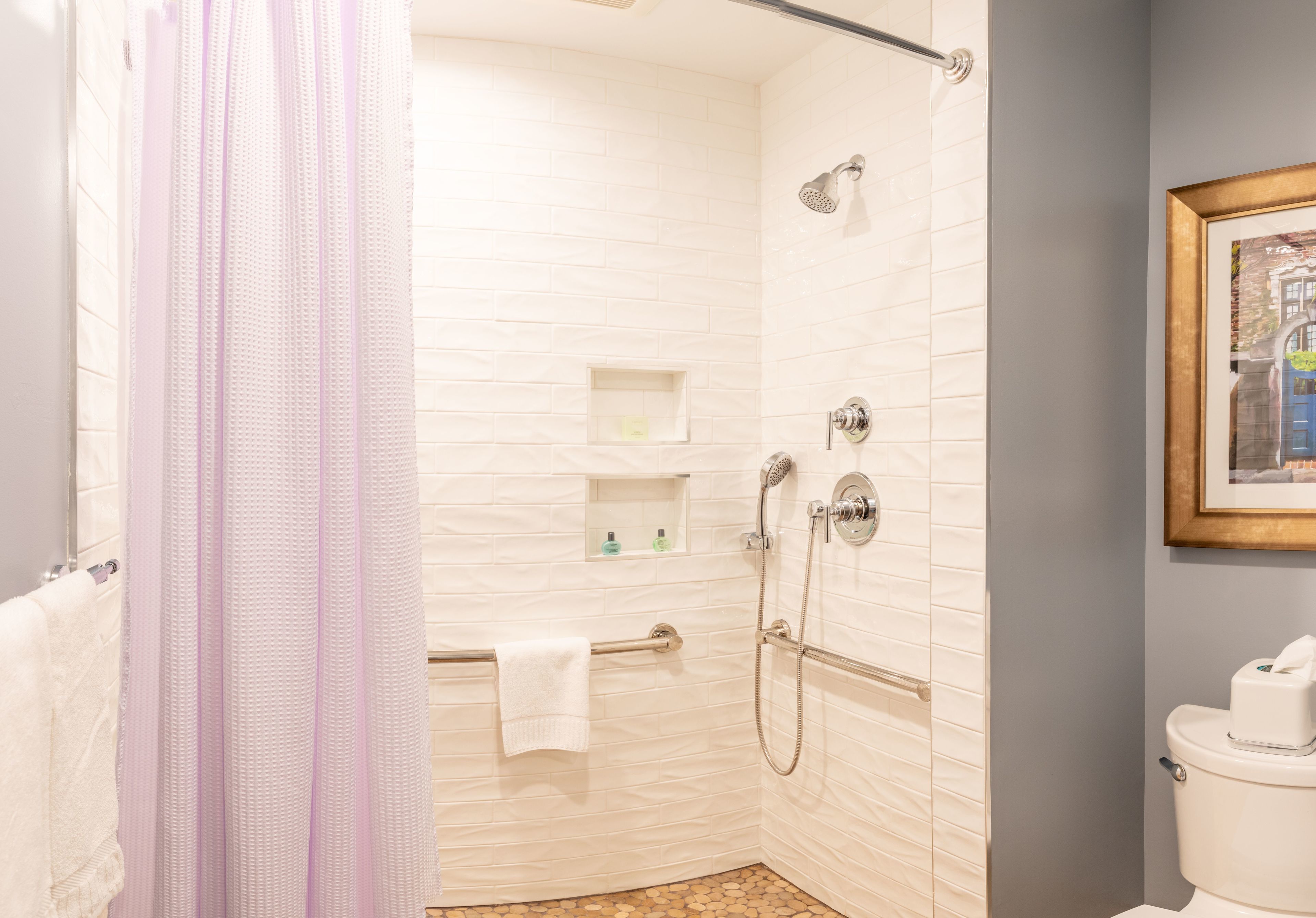 A bathroom with a shower, toilet, and a framed picture on the wall.
