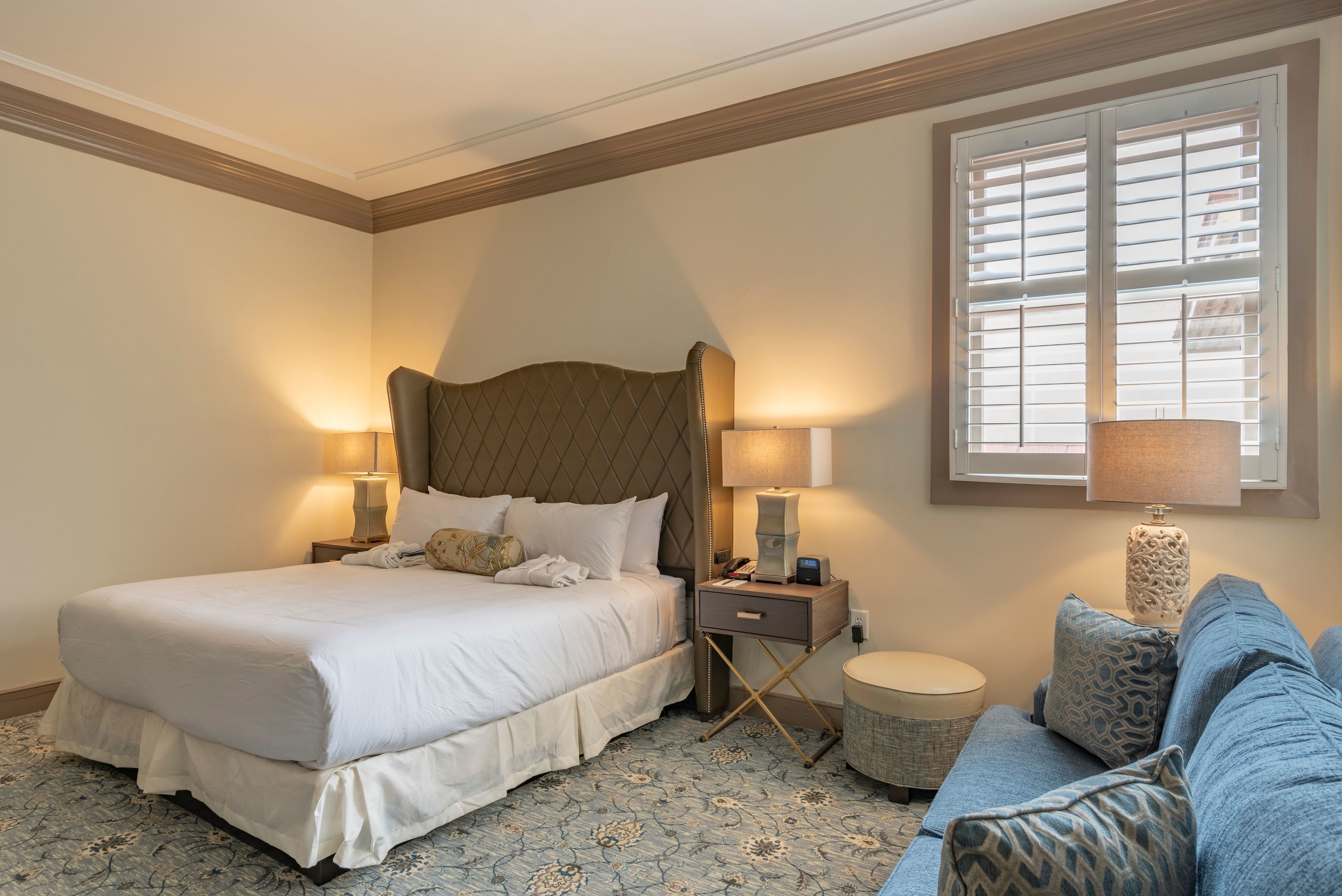 A hotel room with a large bed, two bedside tables with lamps, a small round table, and a blue sofa.